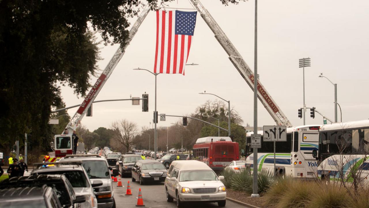 Firetrucks hoist American flag over road.