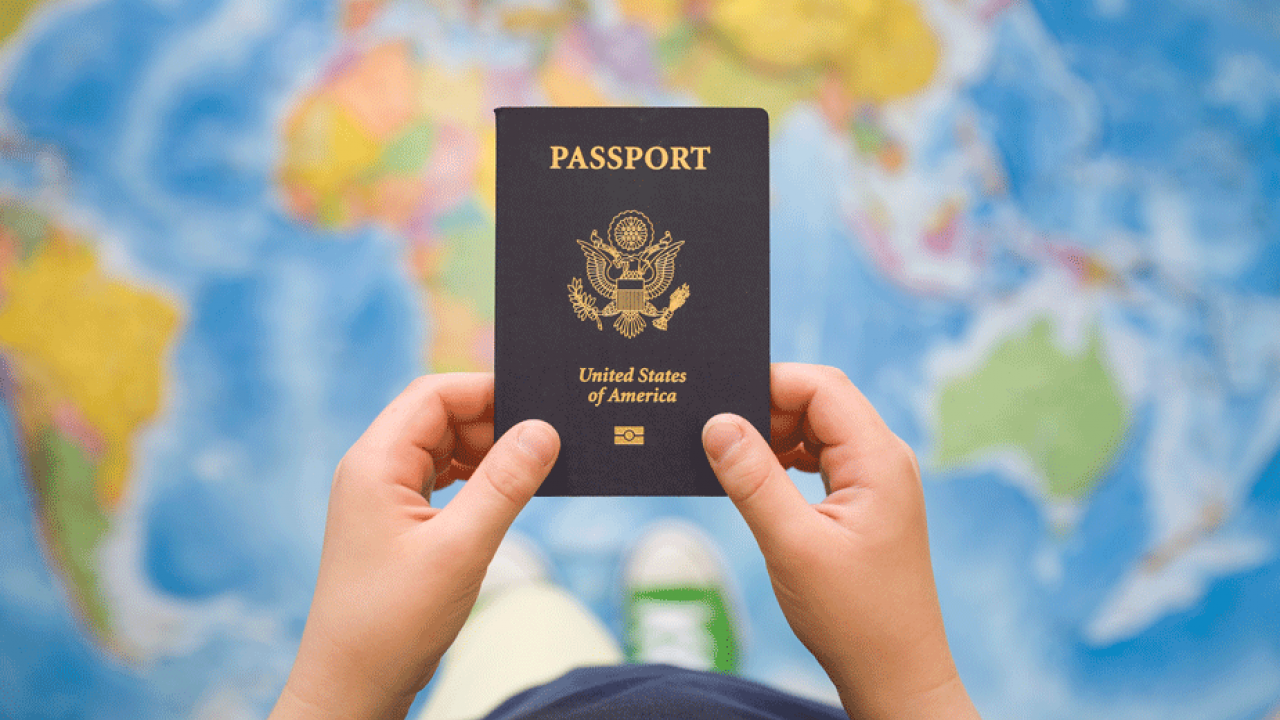 A person holds U.S. passport against backdrop of world map.