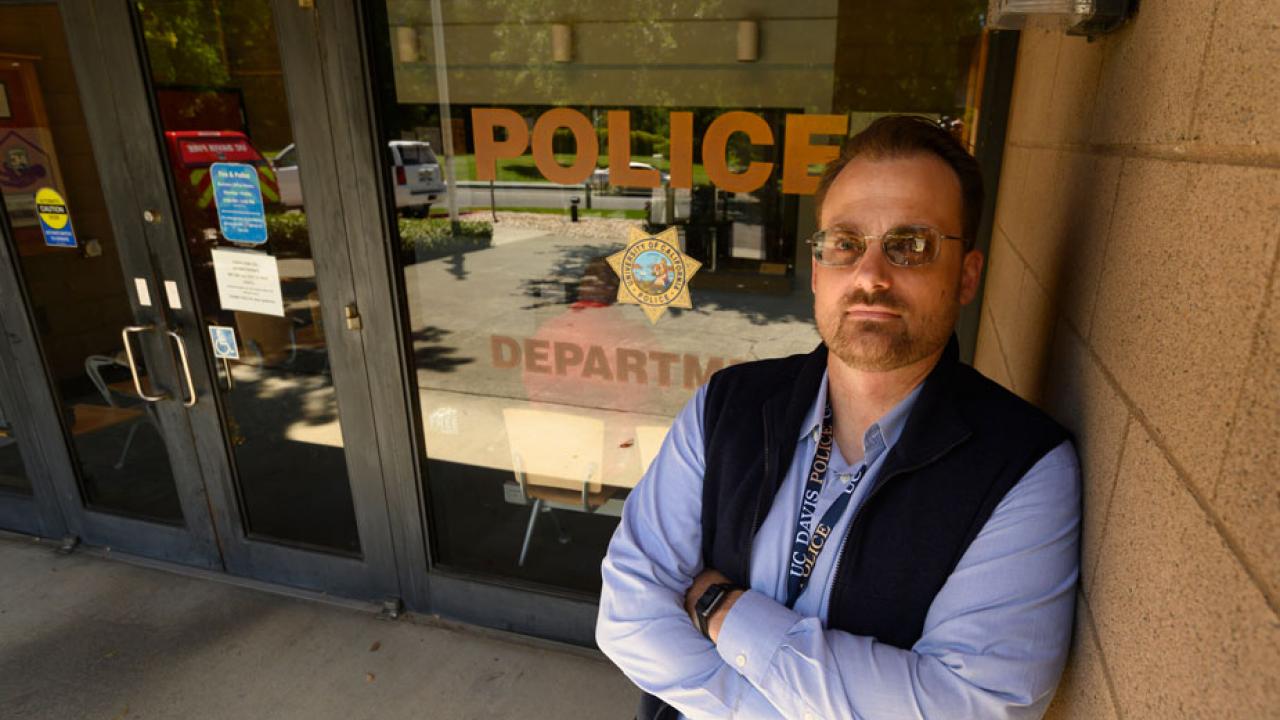 James Bronson stands outside police building, "Police" sign on window, in background.