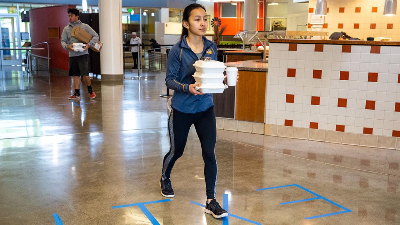 Student walks out of dining commons with takeout containers.