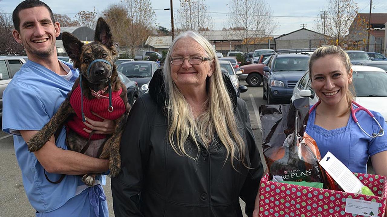 A man holding a German shepherd-mix puppy stands next to a woman in a black coat and a woman holding a large box of dog supplies