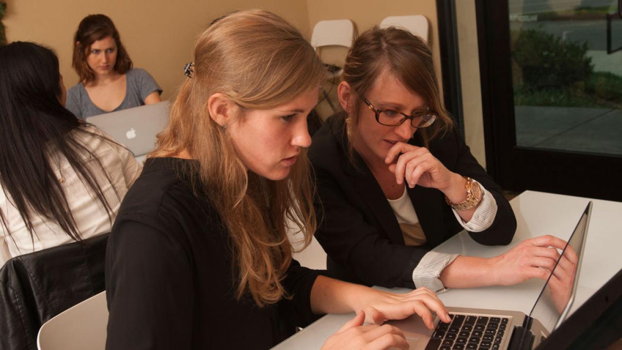 Female student at a computer getting advice from a woman next to her