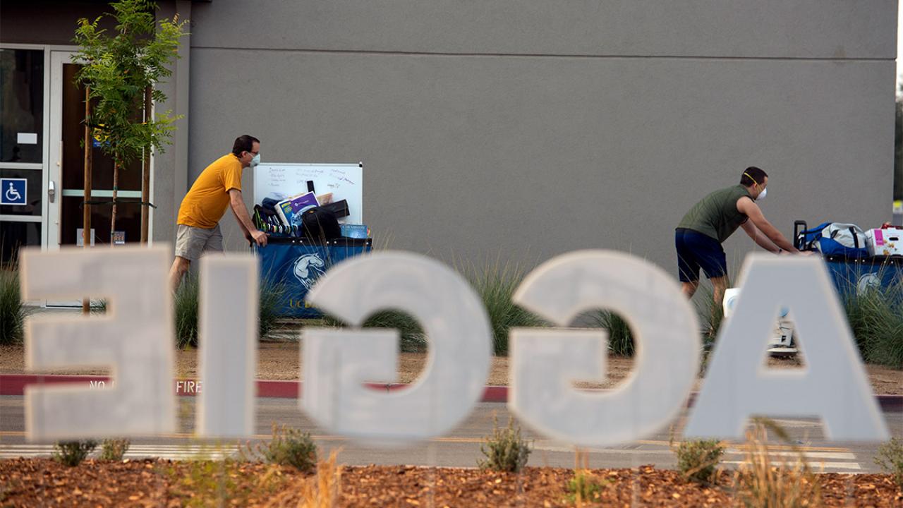 Sign reading "Aggie" with people moving carts in the background.