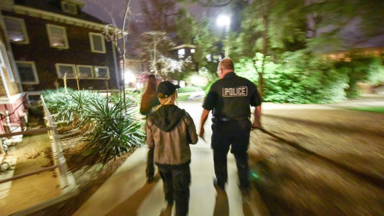 Police officers and two others walk along a campus path at night.