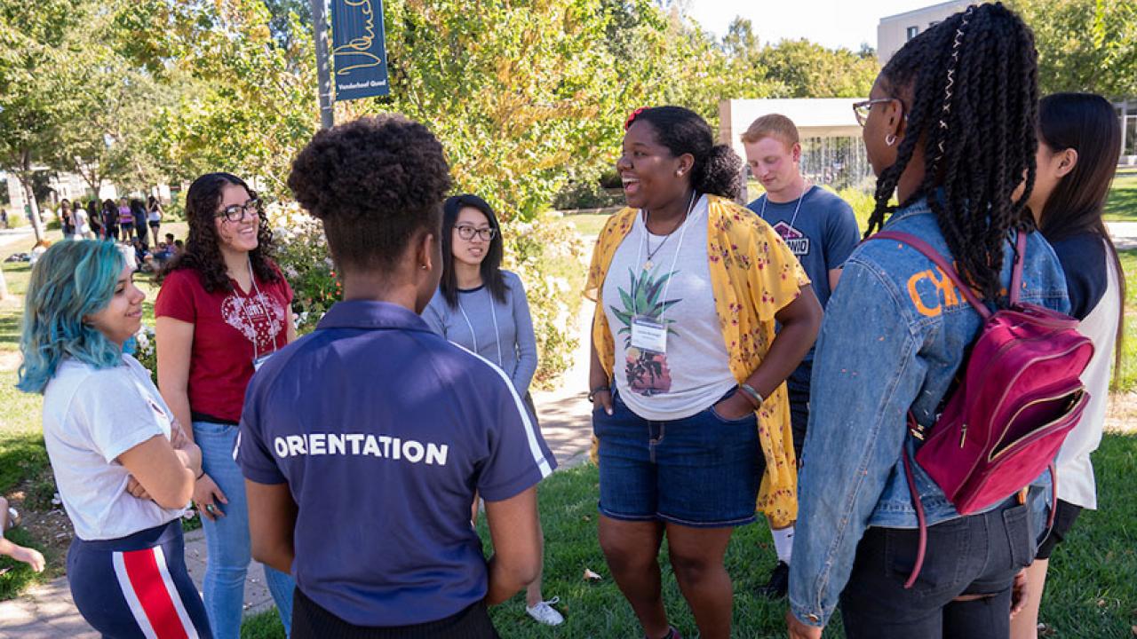 An orientation leader stands with a group of incoming students outdoors.