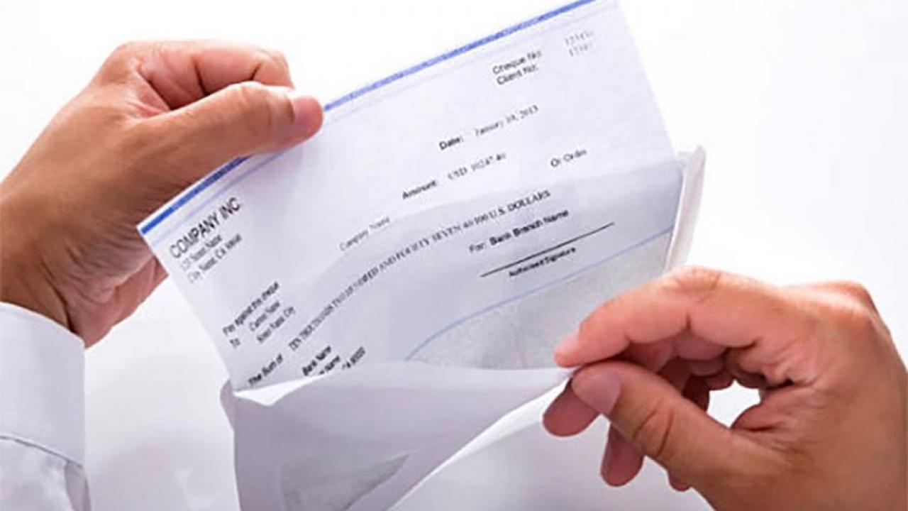 Hands pull paper paycheck from envelope.