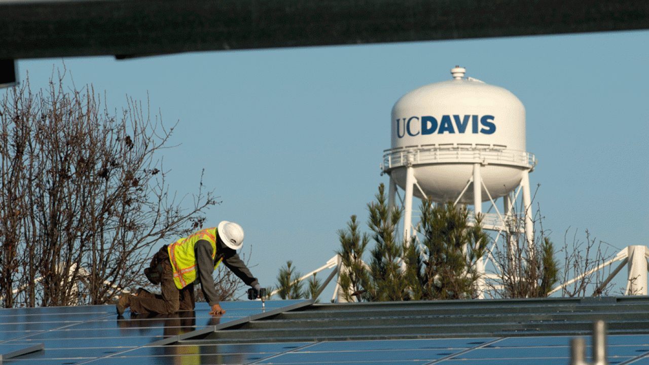 Worker installs solar panels on carportlike structures, in show of UC Davis water tower.