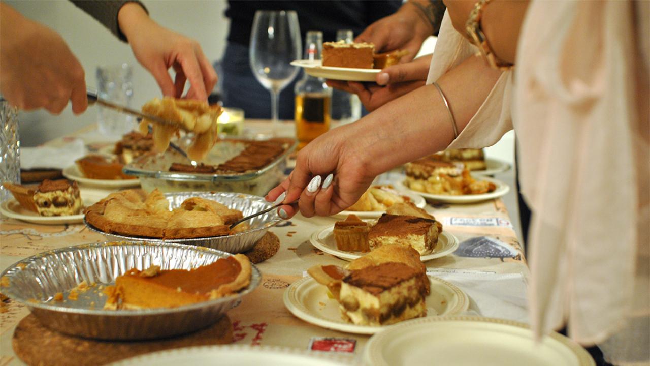 People serve slices of pie from a table.
