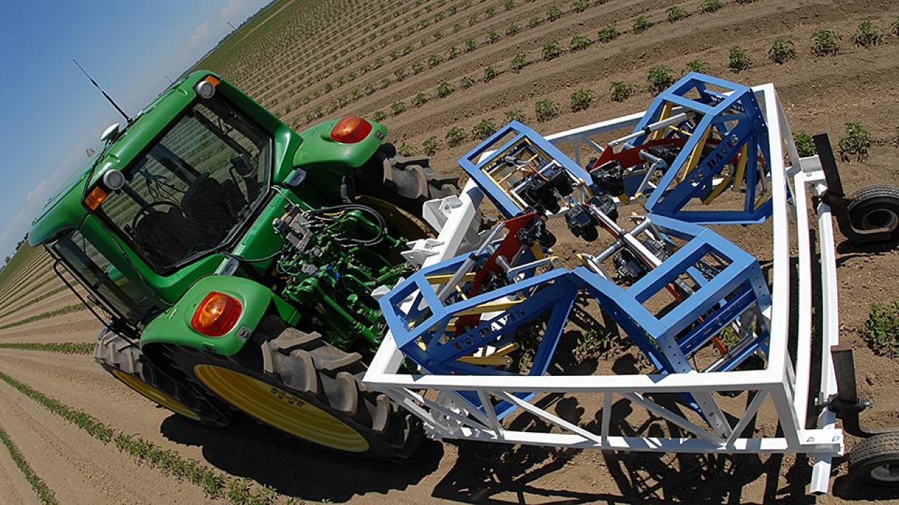 Large tractor pulls frame-like equipment with cameras through tomato field.