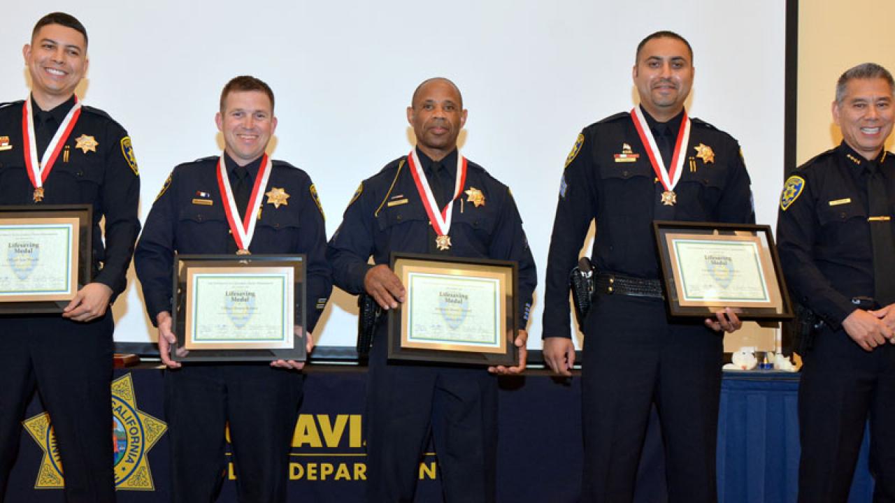 Four police officers in uniform, wearing medals and holding certificates; posing with police chief.