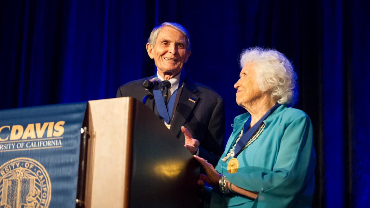 Couple wearing medals hanging from blue ribbons, at UC Davis podium
