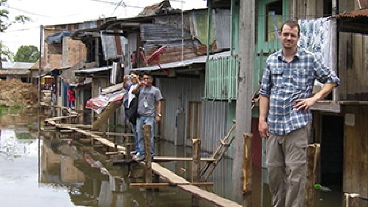 People standing on boards over a river with shacks behind them