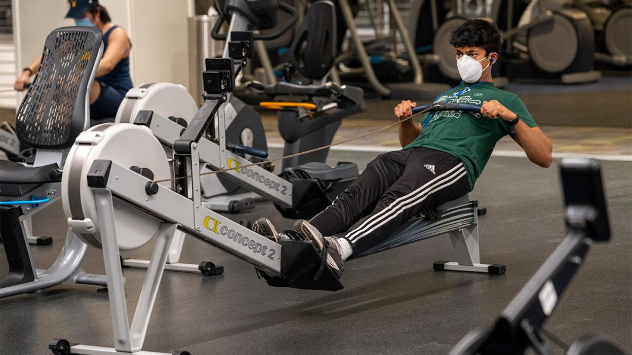 Man wearing face covering uses rowing machine at the ARC.