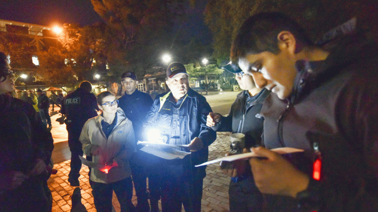 Photo: Police officer surrounded by students, at night, with flashlights, taking notes.