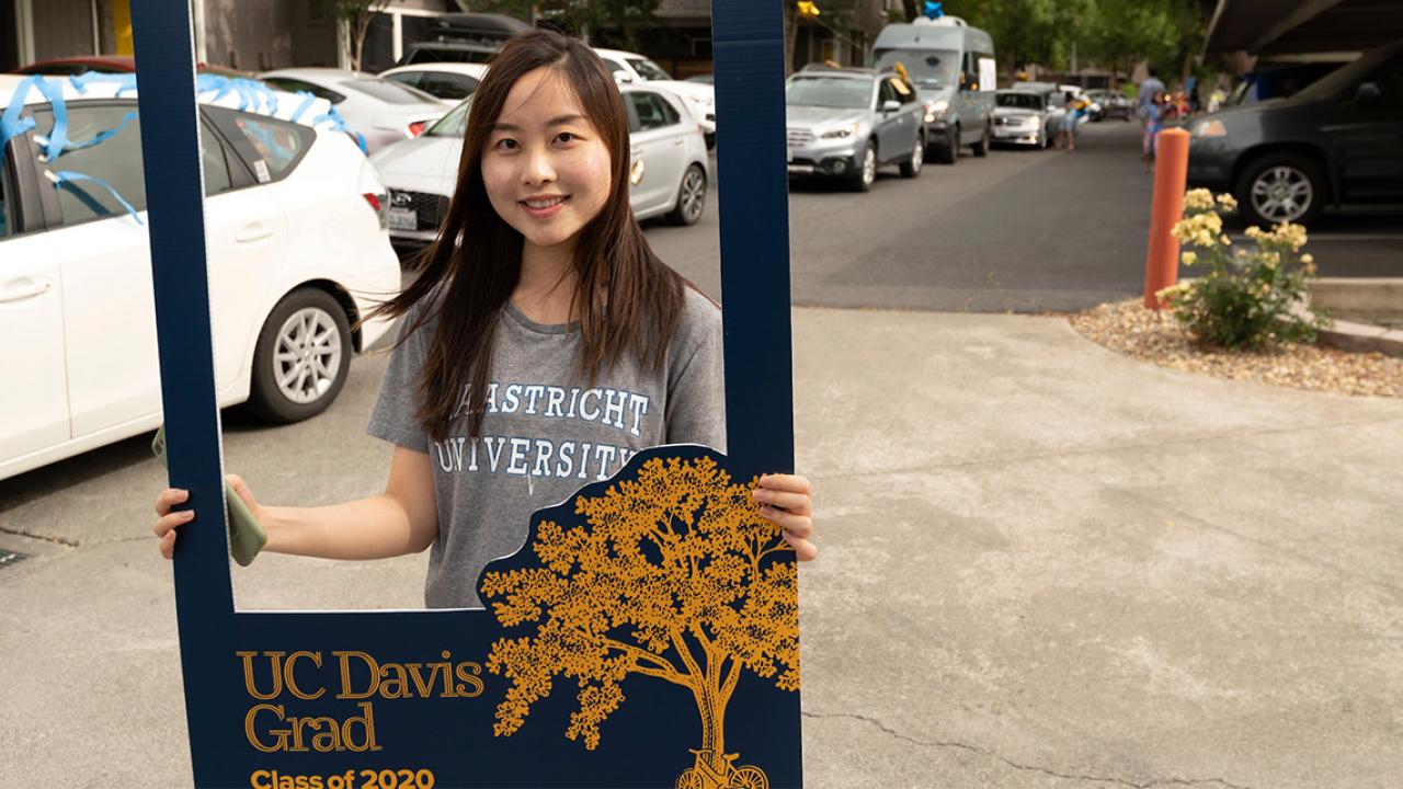Student holds photo frame while row of cars drives past.