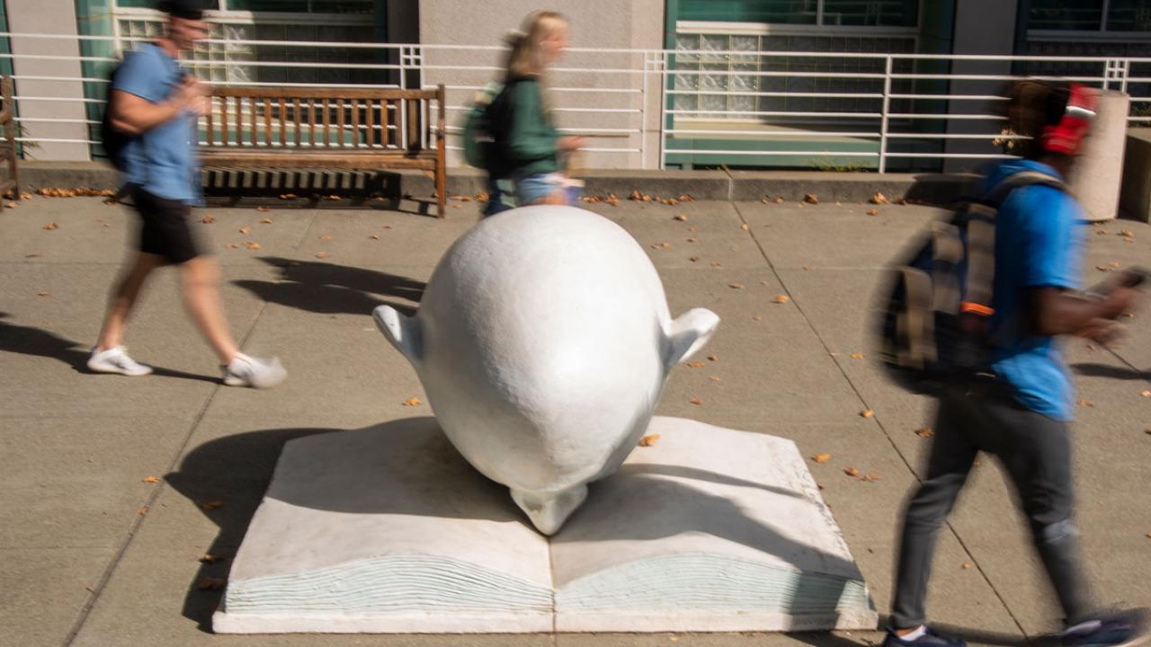 Students (blurred) walking past "Bookhead" sculpture (in focus).