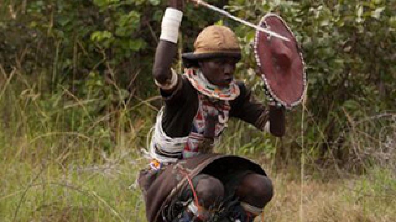 Man in African costume with spear and shield jumping in the air