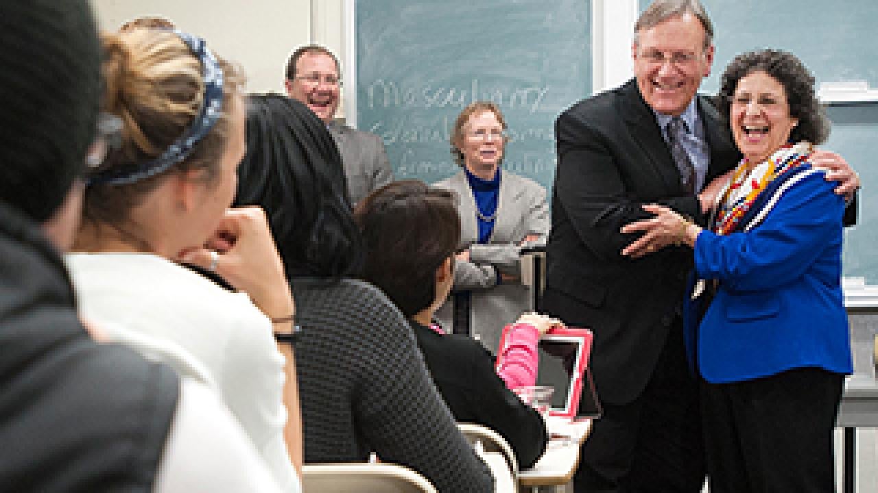Classroom setting showing students seated and man hugging woman in the front