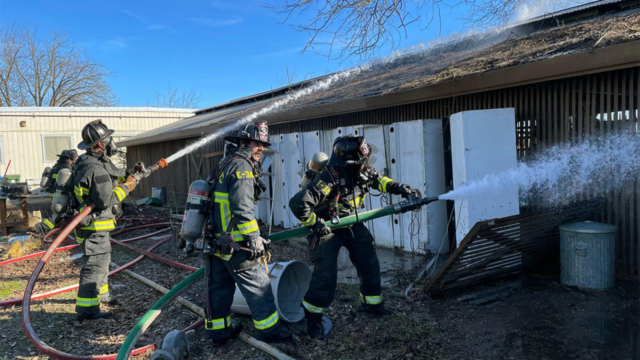 Three firefighters spray water on a building.
