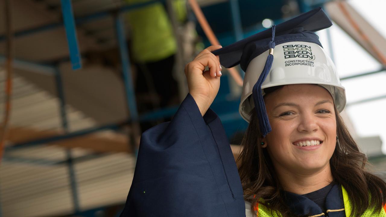 Maria Mu&ntilde;oz in graduation robe and hard hat at a construction site