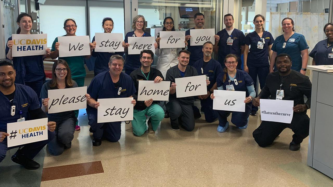 Hospital workers with signs reading "we stay here for you, please stay home for us"