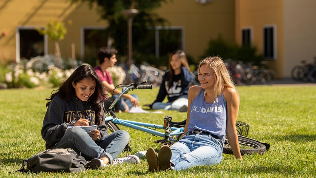 Students sit on the grass in front of a residence hall. 
