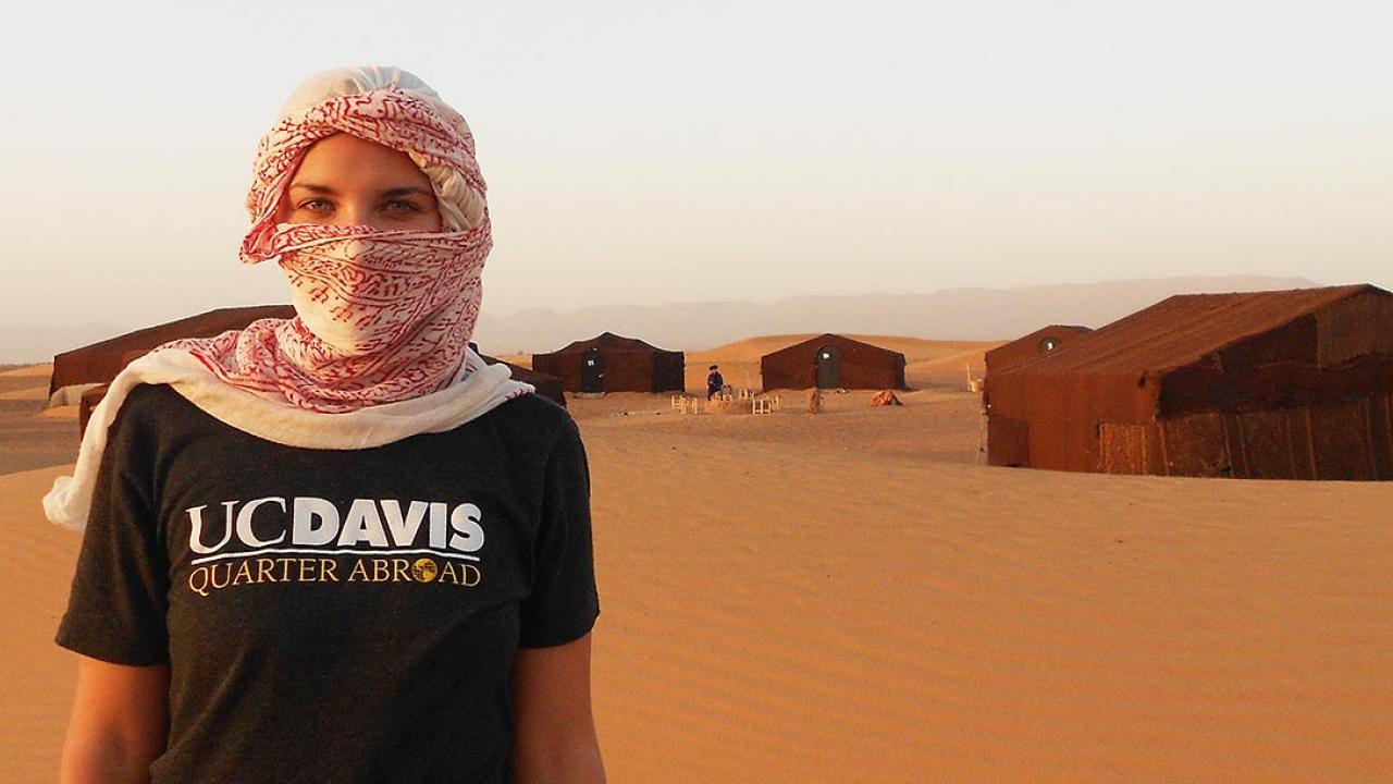 Woman wearing headscarf and UC Davis Quarter Abroad shirt while standing in a desert