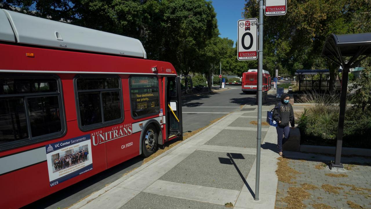 Unitrans bus makes a stop; passenger on sidewalk wears a mask.