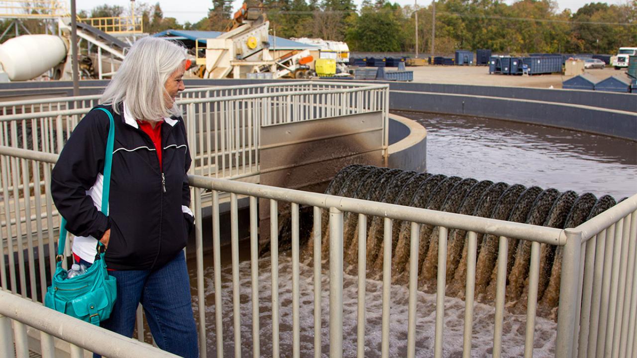 Woman walks past wastewater treatment plant tank.