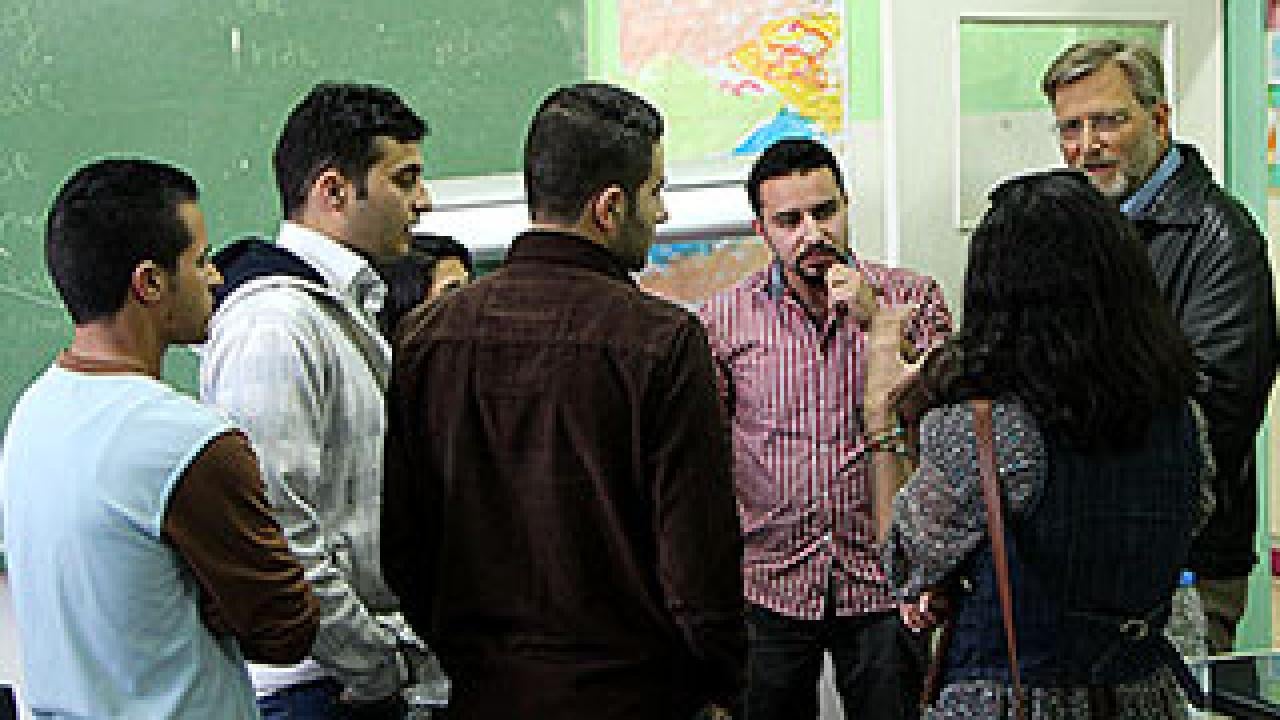 A group of men and one woman talking to a man in a beard in a classroom