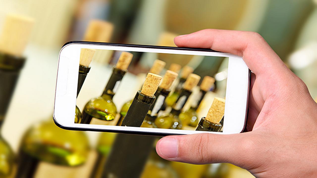 A hand-held cell phone captures an image of wine bottles with corks