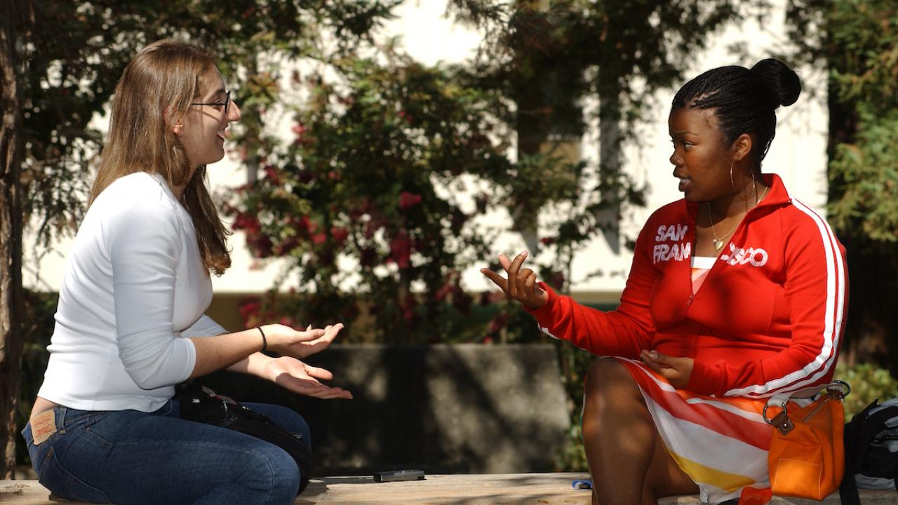 Two female students discuss the classwork outside of Wellman Hall
