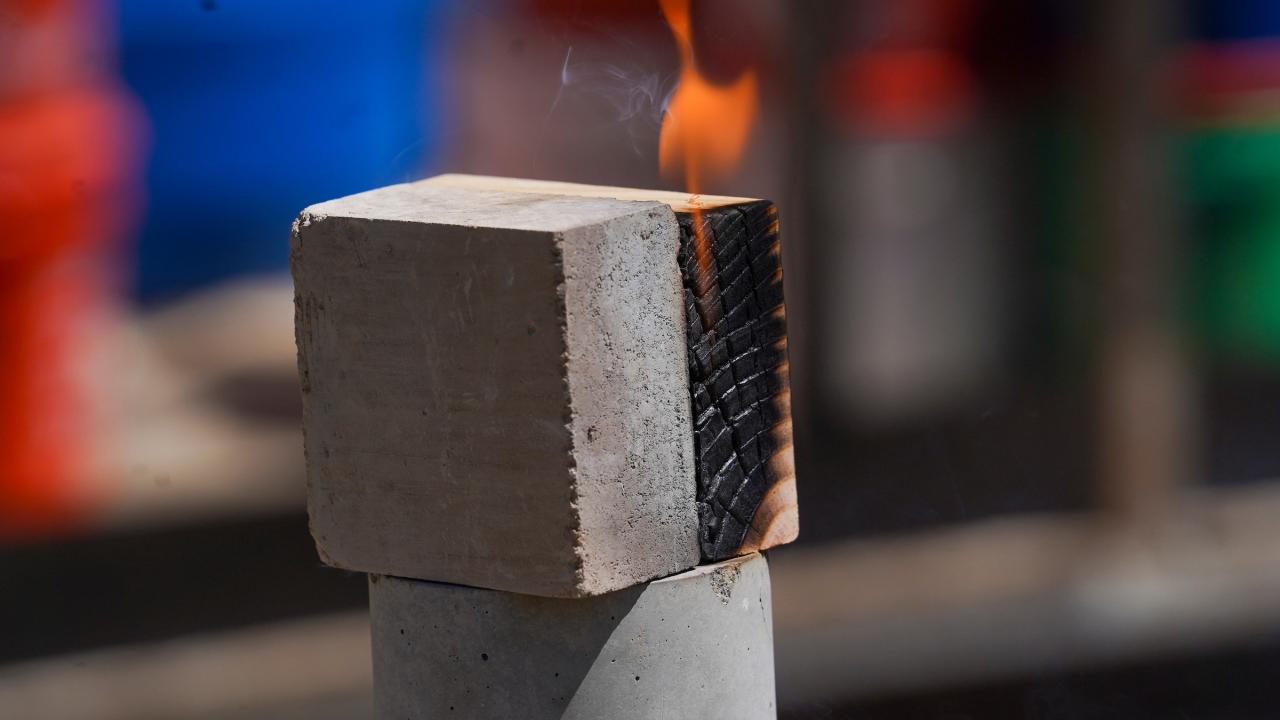 An earth block sits next to a block of wood, with a flame of fire coming from the charred wood after being blowtorched. 
