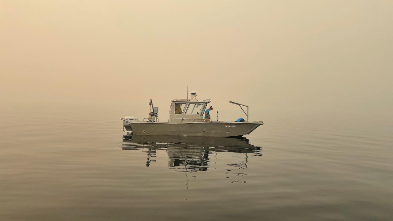 Researcher Brandon Berry from the UC Davis Tahoe Environmental Research Center collects data from a research vessel on the water at Lake Tahoe amid smoke-filled skies. 