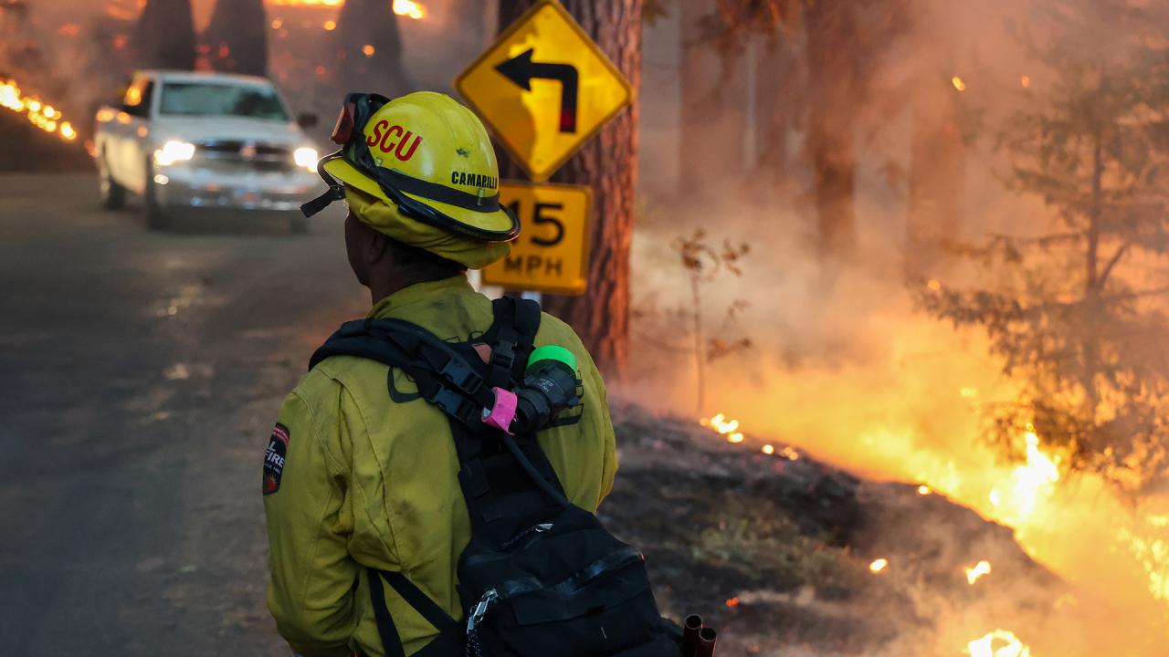 Firefighter in yellow firefighting gear walking toward a wildfire
