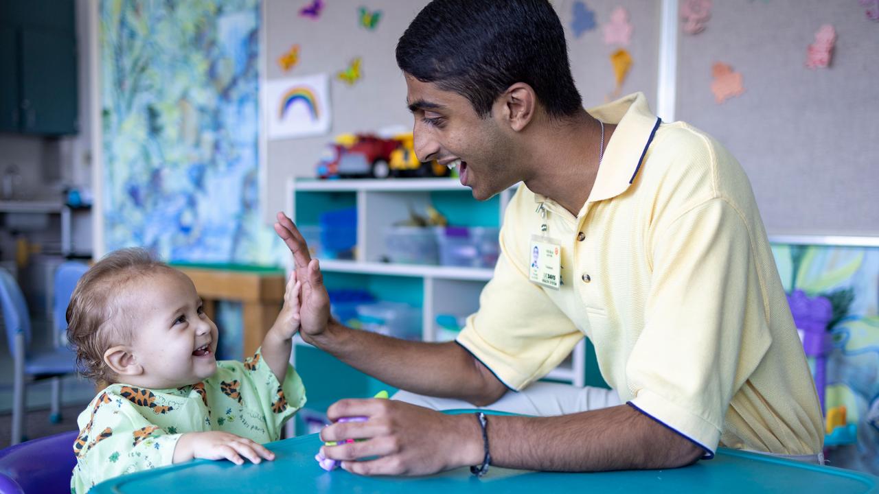 Neeraj Senthil and a toddler share a high 5 in a playroom at UC Davis Children's Hospital.