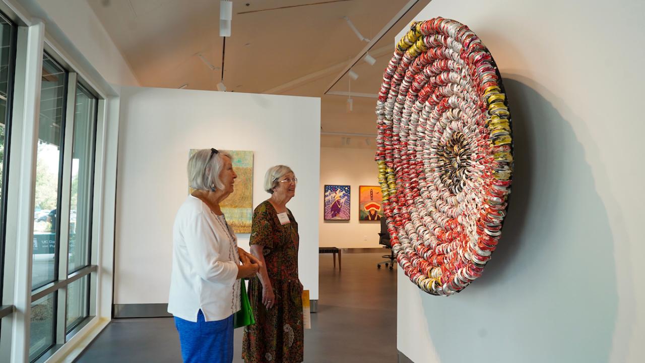 Two museum visitors look at artwork of smashed cans displayed at Gorman Museum of Native American Art