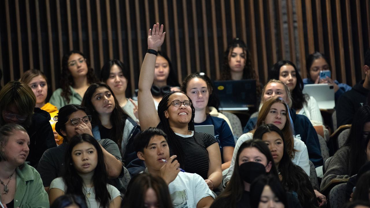 Surrounded by other students, a student raises her hand in class