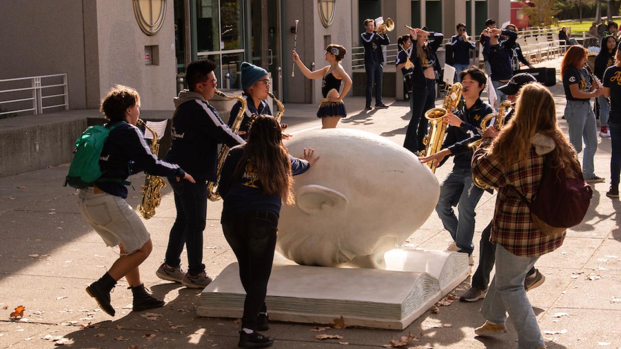 students celebrate around Bookhead, the egghead sculpture by the library on UC Davis