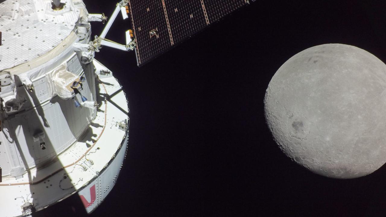 Photo taken in space with part of a spacecraft on the left and the moon on the right. 
