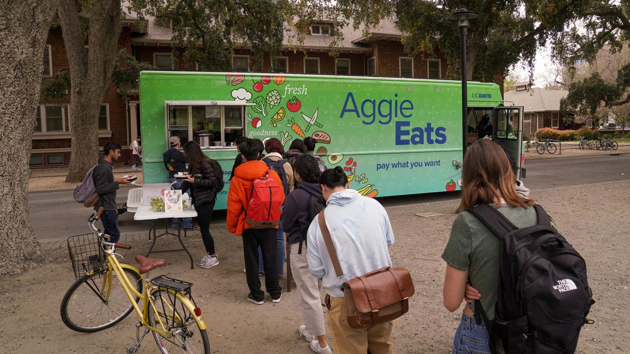Students line up in front of the bright green Aggie Eats food truck parking on the side of the Quad.