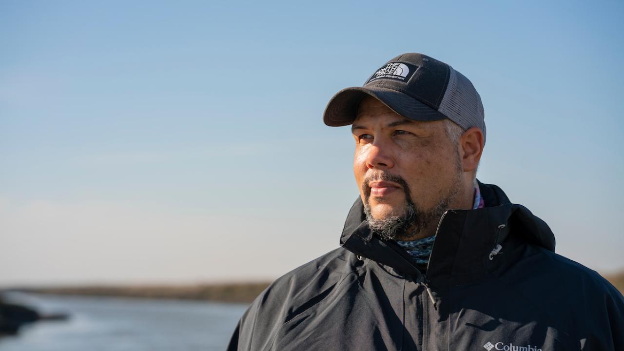 Levi Lewis in ball cap and blakc jacket with backdrop of Alviso slough in California
