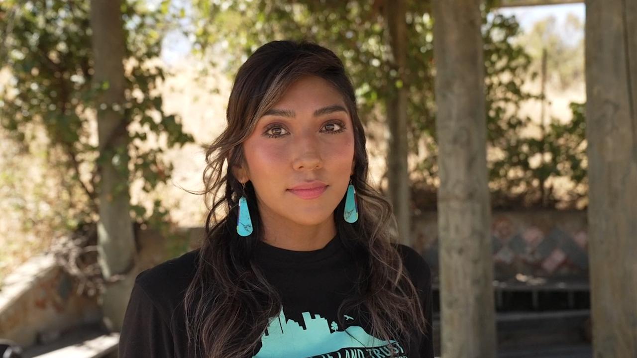 Native America woman in black shirt and blue earrings looks directly at camera for a series on climate anxiety. 