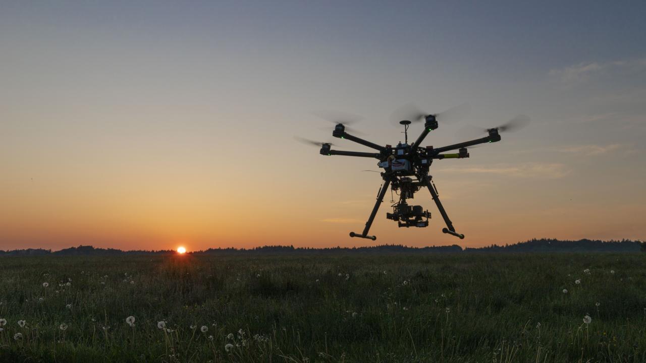 drone flies over open field at sunset