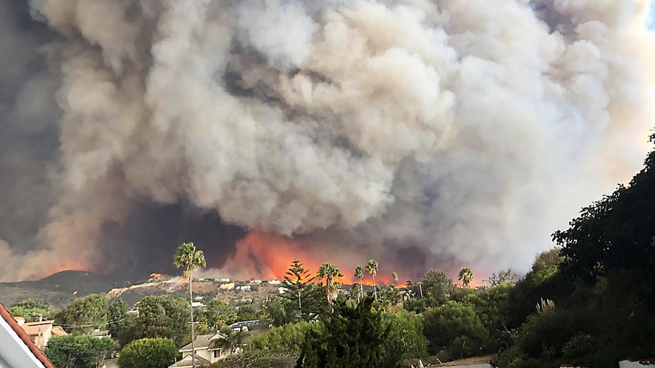 Wildfire smoke from the Woolsey Fire in 2018 billows behind trees and houses in Malibu, California. 