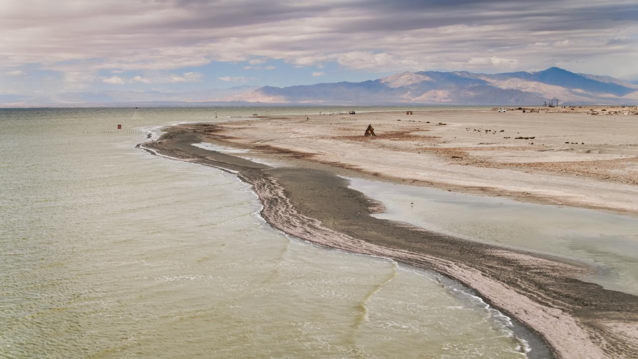 drone image of Salton Sea waters going up to dry lakebed with mountains in distance