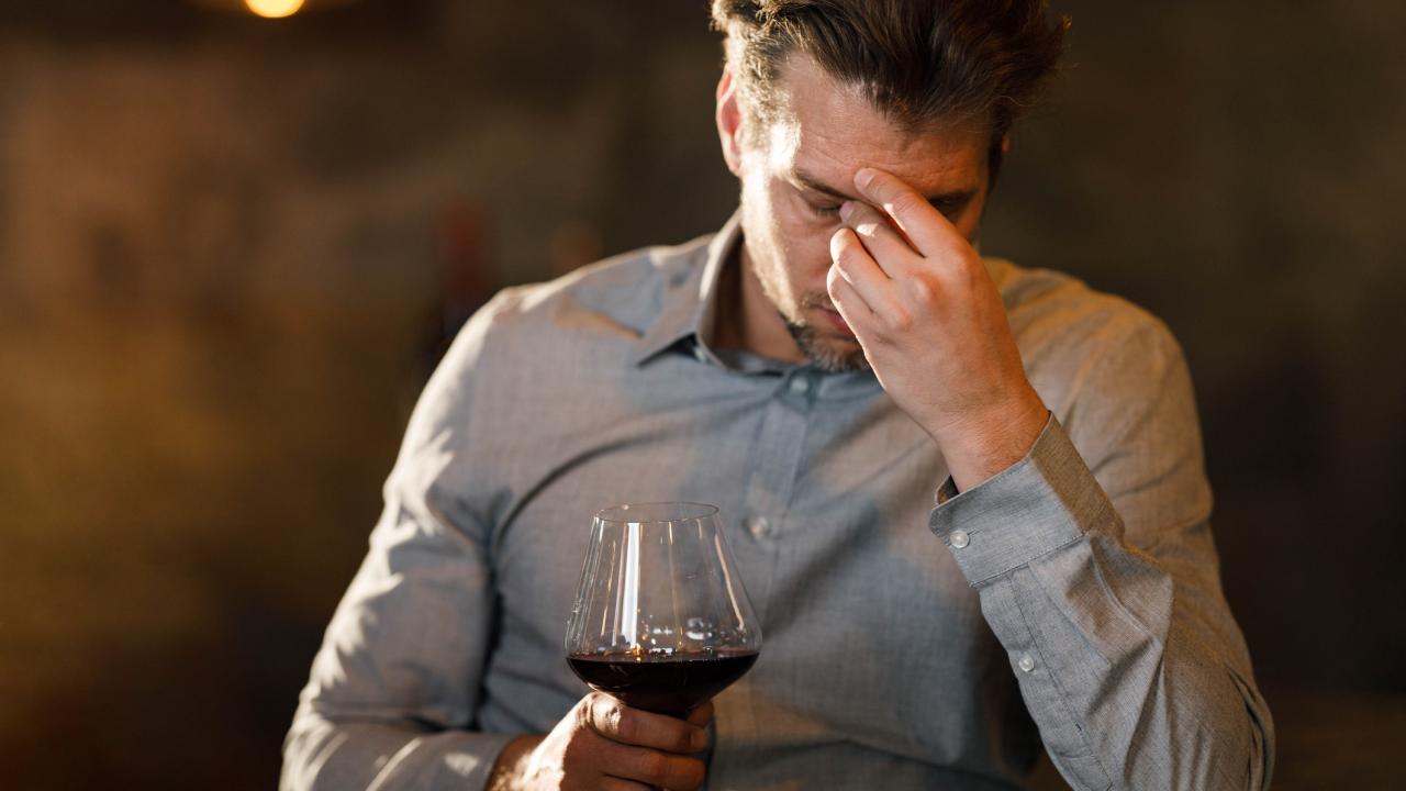 Man rubbing his forehead while drinking red wine. UC Davis scientists theorize that a flavanol found naturally in red wine can interfere with the metabolism of alcohol and cause "red wine headache." (Getty)