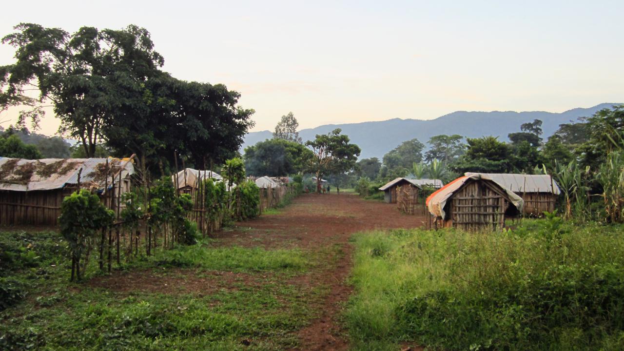 Looking down the middle of an African village with wooden buildings and mountains in the distance.
