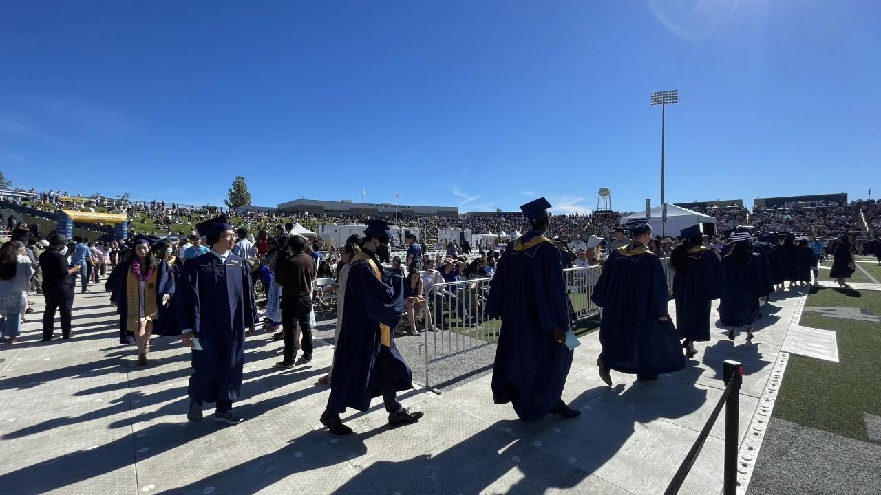 UC Davis graduates walk in cap and gown at sunny commencement