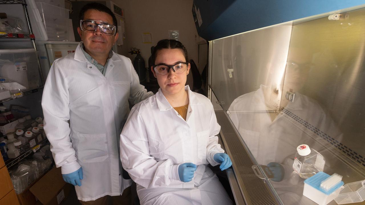 Wearing white lab coats, Jasmine Diaz and Luis Carvajal-Carmona pose in a science lab